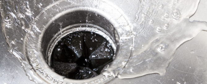 close up image of a garbage disposal in a stainless steel sink with water flowing down it